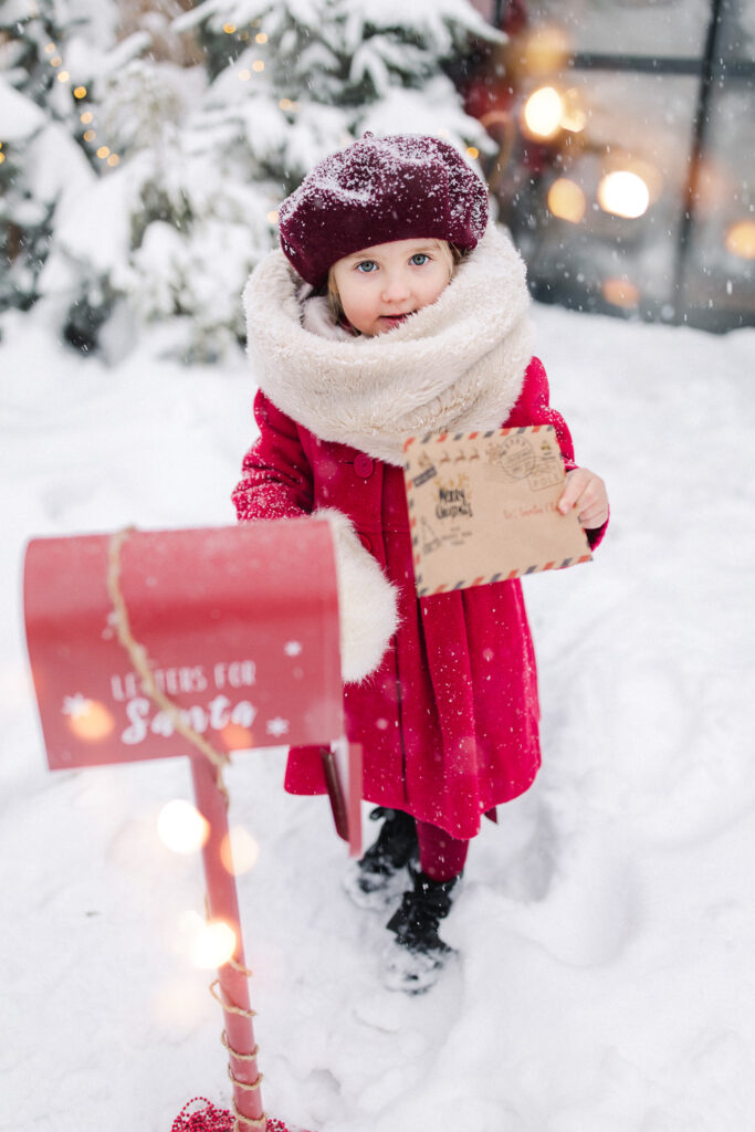 Dziewczynka w zimowej stylizacji podczas sesji świątecznej w Szklarniowe Love w Żywcu – ciepła czapka, bordowy płaszczyk i śnieżna sceneria